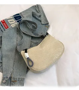 Close-up of beige corduroy crossbody bag texture with striped strap on denim jacket