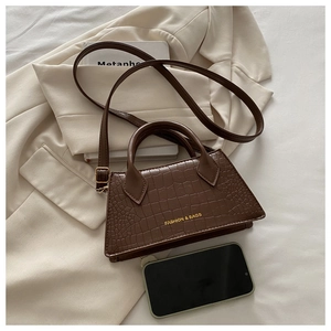 Detail of dark brown crocodile texture handbag showing size relative to a smartphone