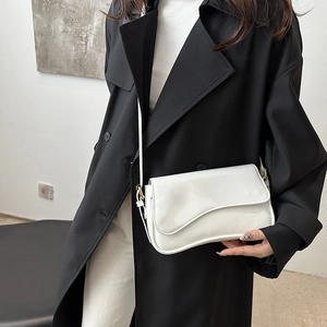 White glossy patent leather baguette shoulder bag with stylish wavy flap design worn by model