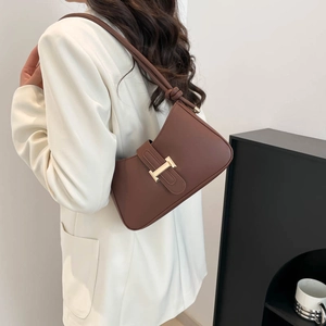 Sac sous le bras en cuir marron avec boucle H dorée porté sur une veste blanche
