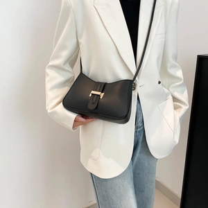 Sac sous le bras noir avec boucle en métal doré porté sur un blazer blanc