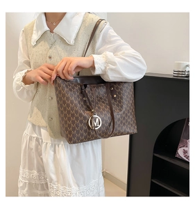 Detailed view of brown tote bag with repeating M patterns and golden metal charm