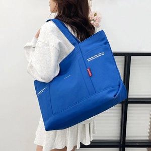 Blue canvas tote bag with white lettering and red label shown on shoulder by model