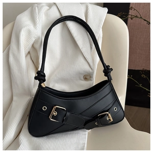 Black half-moon shoulder bag with gold buckles and knotted strap on a white blazer