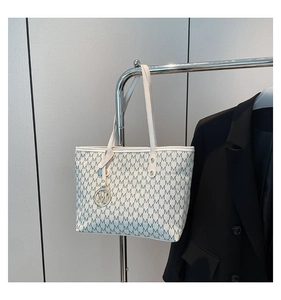 Detail view of white tote bag featuring black M-pattern print and metallic M-charm