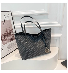 Detailaufnahme der großen Tote-Bag mit M-Muster und Metallanhänger auf weißem Sockel