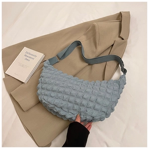 Detail of light blue bubble textured crescent shoulder bag with wide strap on beige fabric