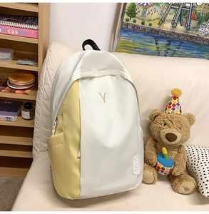 Detailed close-up of color-block nylon backpack with letter embroidery on ivory surface