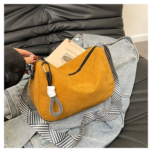 Detail of yellow corduroy crossbody bag featuring a striped wide strap and charm