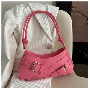 Close-up of pink baguette bag with decorative straps and gold buckle on a chair