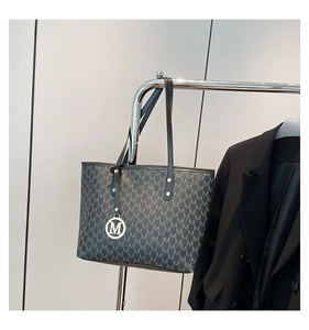 Detail of black tote bag with gray M-pattern print and silver M-logo pendant charm
