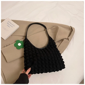 Detail of black textured bubble tote bag featuring a green flower charm and sleek strap