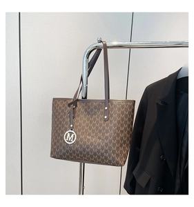 Detailed macro view of brown leather tote bag featuring monogram print and metal M charm
