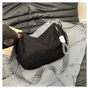 Detail of black corduroy hobo bag with striped strap on denim background