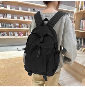 Rear view of a black nylon unisex backpack shown in a quiet library setting