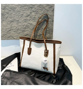 Detail view of large white tote bag with brown straps and a plush monster charm