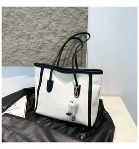 Detail of minimalist tote bag with contrast piping and a fuzzy monster charm accessory