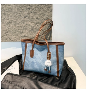 Detail of blue denim tote bag with brown leather straps and plush white doll pendant