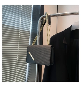 Detail of black crossbody bag with diagonal texture and gold chain hanging on a metal rack