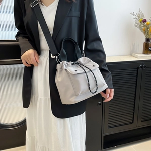 Minimalistische beige Nylon-Beuteltasche mit schwarzem Gurt in Lifestyle-Szene