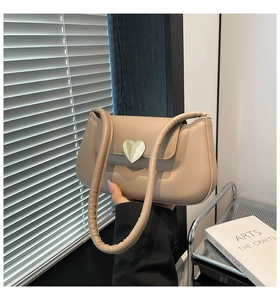 Detail of a minimalist beige leather shoulder bag featuring a gold heart-shaped metal lock