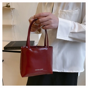 Borsa tote rosso scuro con logo portata da una modella in un ambiente dallo stile minimal