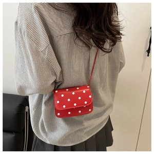 Close-up of red crossbody square bag with white polka dots shown on a model