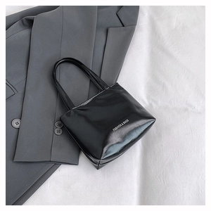 Dettaglio di una borsa tote nera con texture in vernice lucida e stampa del logo bianco