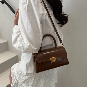 Retro brown glossy leather handbag with gold square buckle shown on a white lace dress