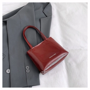 Dettaglio della borsa tote bordeaux lucida con scritta su sfondo di colore neutro