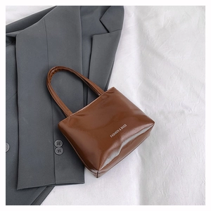 Dettaglio borsa tote in pelle verniciata marrone con testo bianco su blazer grigio