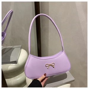 Detailed view of lavender baguette bag with gold bow clasp on a reflective surface
