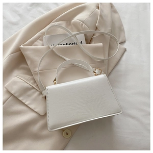 Detail of white rectangle handbag on beige blazer featuring light gold hardware and fine texture