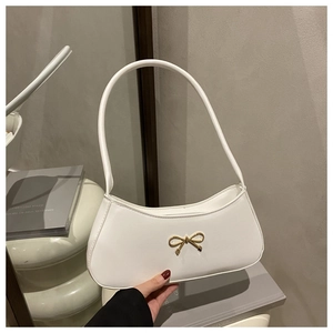 Close-up of white baguette shoulder bag with elegant gold bow hardware and leather texture