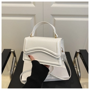 Detail of white minimalist handbag with wavy flap edge and pale gold hardware