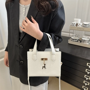 Sac tote blanc à motif litchi avec fermoir doré et pendentif cerf sur un mannequin