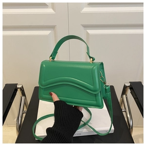 Detail of green handbag showing wavy flap design and gold hardware with a top handle