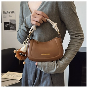 Detail of a brown half-moon leather bag featuring white knotted handle and monster charm