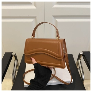 Detail of a brown leather square bag with wave flap design and gold metal buckle