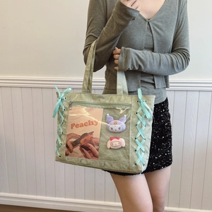 Light green ita tote bag with clear window and blue ribbon details on a model