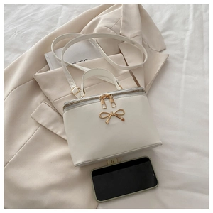 Détail d'un sac boîte crème avec nœud doré et bandoulière posé sur un blazer beige chic