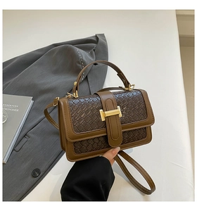 Detail of hand-woven leather texture and gold H-buckle on a brown square handbag
