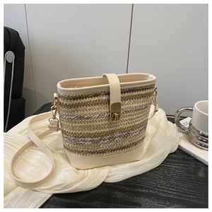 Dettaglio della borsa a secchiello in paglia con finiture in pelle crema e chiusura dorata
