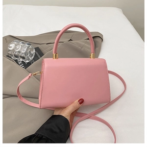 Detailed view of pink trapezoidal handbag with golden cylindrical strap connectors