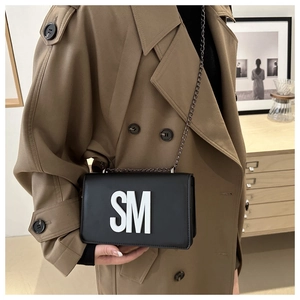 Détail d'un sac bandoulière chic en cuir noir avec logo SM blanc et bandoulière chaîne