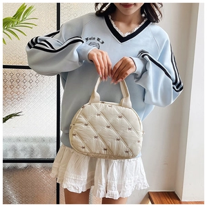 Détail du sac à main matelassé crème avec broderie de nœuds bruns tenu à la main