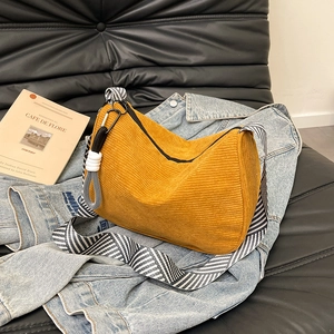Yellow corduroy half-moon bag with striped strap on blue denim jacket and leather sofa