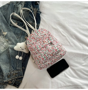 Detail eines geblümten Mini-Rucksacks aus Nylon mit einem Plüsch-Wolken-Anhänger auf Bettzeug