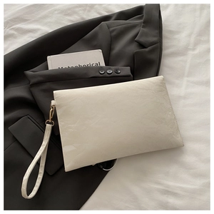Flat lay of cream textured envelope clutch bag on grey suit jacket with golden hardware