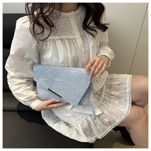 Detail of light blue cloud clutch with gold metal trim held by model in white dress